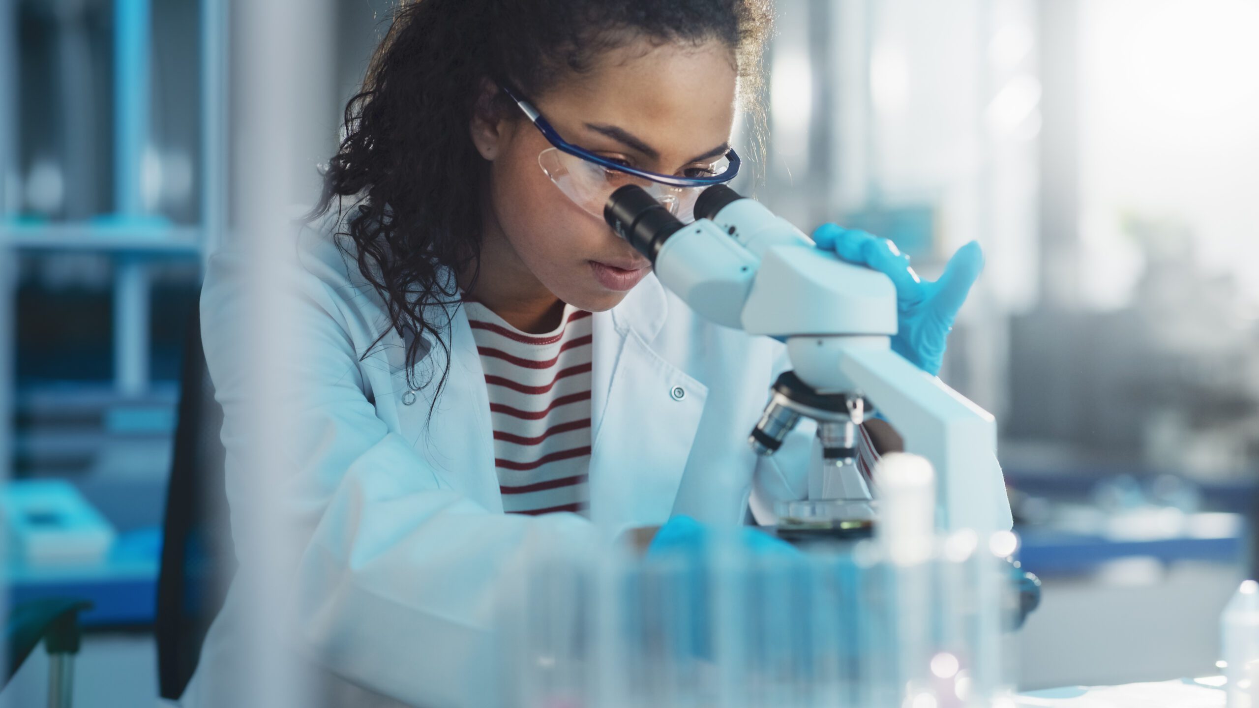 Image of a woman wearing a lab coat, peering into a microscope